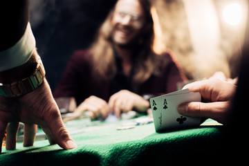 selective focus of man touching playing cards near happy player on black with smoke