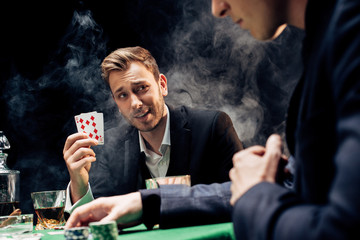cropped view of man playing poker near player on black with smoke