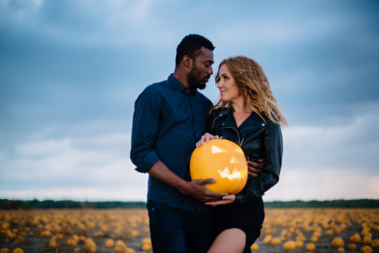 couple standing in pumpkin field and holding scary face pumpkin, concept halloween
