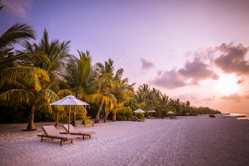 Sunset beach landscape. Luxury vacation and holiday concept, summer travel banner. Panoramic landscape of sunset beach, two loungers umbrella, palm leaf, colorful sunset sky for paradise island view