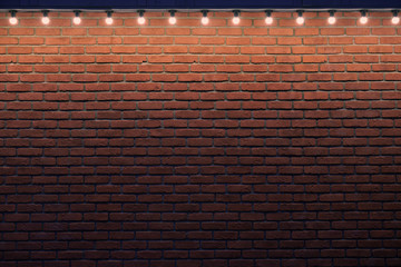 An orange brick wall with small light bulbs. Gradient stone background with low light and copy space. Place for advert.
