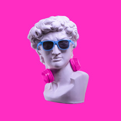 Fototapeta Statue. Earphone on a pink background. Gypsum statue of David's head. Creative. Plaster statue of David's head in blue sunglasses. Minimal concept art. obraz