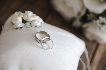  silver wedding rings on a white silk pillow with roses on a wooden surface with roses in the background