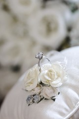 diamond wedding ring on a white silk pillow with roses in the background