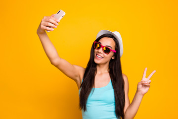 Photo of cheerful cute charming nice fascinating girl showing you v-sign recording video taking selfie wearing cap sunglass isolated over yellow vivid color background