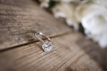  diamond wedding ring on a wooden surface against the background of a bouquet of flowers