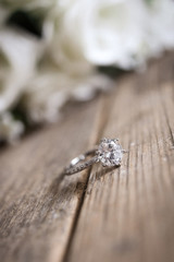  diamond wedding ring on a wooden surface against the background of a bouquet of flowers