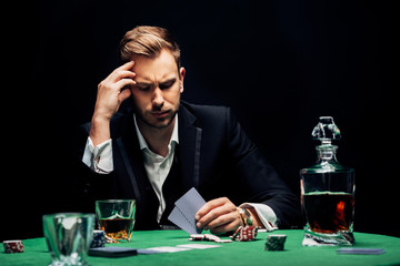 selective focus of upset man holding playing cards isolated on black