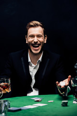happy man holding poking cards and glass with alcohol isolated on black