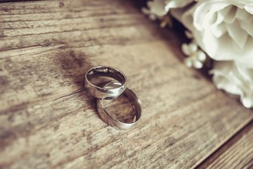 Beautiful toned picture with wedding rings lie on a wooden surface against the background of a bouquet of flowers