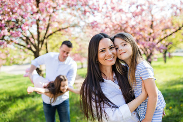 Young parents with small daugthers standing outside in spring nature.
