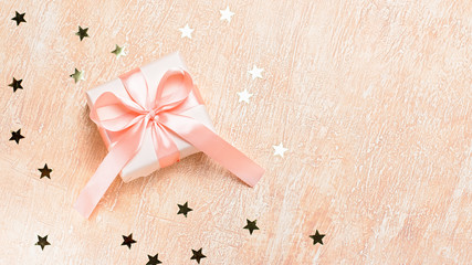 Pink gift box with bow and golden confetti on creative background, copy space. Background for holiday