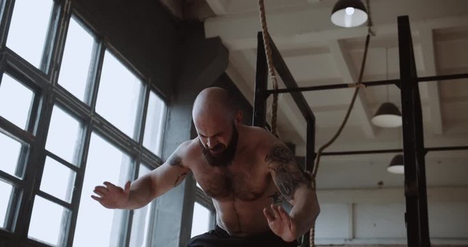 Young strong muscular shirtless Caucasian male athlete doing burpee exercises during functional workout in large gym.