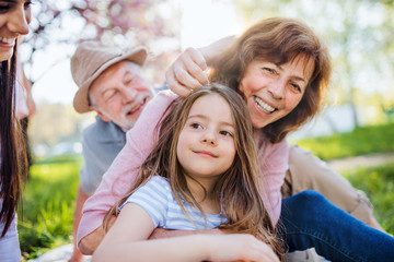 Fototapeta premium Senior grandparents with small granddaugther sitting outside in spring nature.