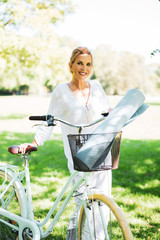 attraktive ältere frau ist mit dem fahrrad im park unterwegs, sie hat eine yoga-Matte dabei 