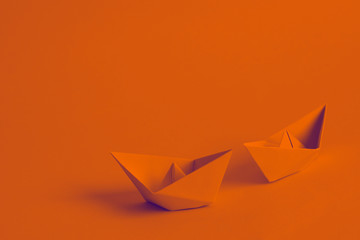 Burnt orange paper boats on orange background. A pair of paper ships that symbolize eternal love...