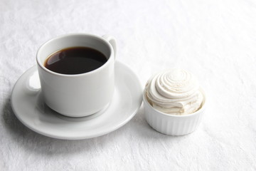 White cup of black coffee and marshmallows on textile cover