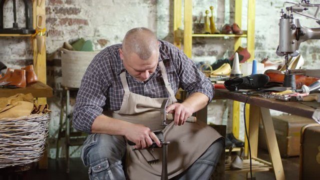 Tracking shot of professional middle aged shoemaker grinding heel tips with machine while repairing female boots in workshop