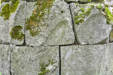 Ancient, built of weathered stone blocks. Background of masonry, overgrown with green moss. Detail of medieval stone build