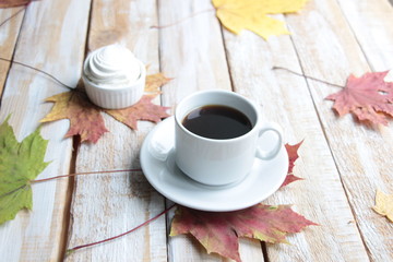 White cup of black coffee and marshmallows on wooden background with colorful maple leaves