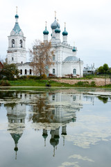Autumn day in traditional Russian village. Autumnal sad landscape with church reflections on the lake