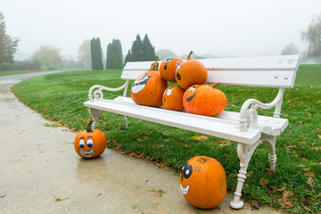 Many pumpinks with painted faces on white porch.
