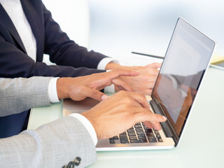 Cropped shot of coworkers using laptop. Close-up partial view of businessman and businesswoman using laptop computer together in office. Technology concept