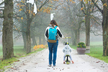Youg mother walking with her daughter riding a toddler scooter in park.