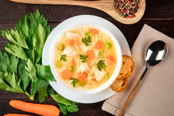 Chicken noodle soup with ingredients on a dark rustic wooden background