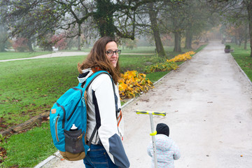 Youg mother walking with her daughter riding a toddler scooter in park.
