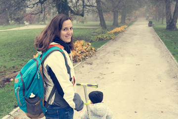 Youg mother walking with her daughter riding a toddler scooter in park.