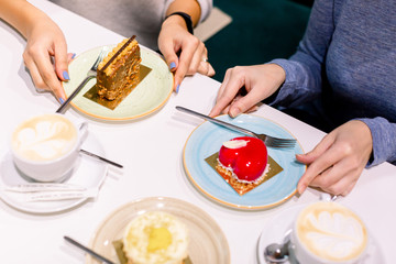 Drinking coffee and eating desserts together. Top view of hands of two beautiful women keeping hands on plates with delicious desserts in cafe. Meeting of best friend. Coffee with cakes