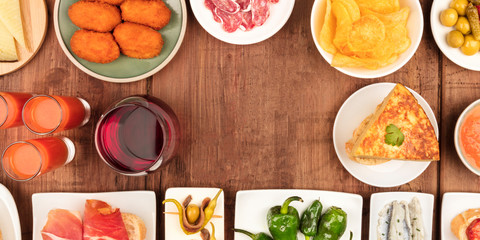 A panorama of Spanish tapas, a variety of snacks, top shot. Gazpacho, tortilla, and wine, shot from above on a dark rustic wooden background with a place for text