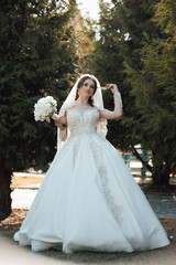 Likable and pretty bride in a white wedding dress with a wedding bouquet in his hands on a enjoying romantic moments outside on a summer. Wedding day.  Dreamy bride hold  beautiful bouquet