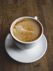 A beautiful cup of cappuccino with latte art in the wooden background. Minimal composition. Copy space for your text.