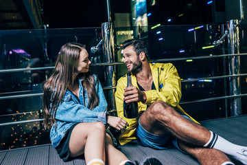 Fototapeta na wymiar handsome boyfriend with bottle and attractive girlfriend smiling and talking in night city