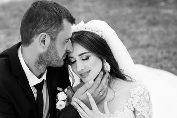 Beautiful bride and groom embracing and kissing on their wedding day outdoors. Black and white