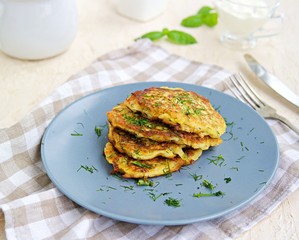 Fritters zucchini with feta cheese on a gray plate on a light concrete background. Served with sour cream. Zucchini recipes. Selective focus.