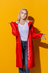 Pretty blond girl in a red raincoat and white t-shirt standing isolated over yellow background. Be bright in bad weather.