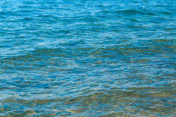 Clear water texture in blue and orange. Background of the ocean and the sea backlit by the sun. Soft waves. Natural water