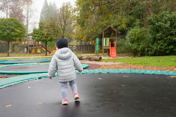 Baby girl standing on a trampoline outdoor.