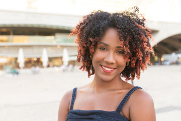 Happy cheerful African American lady posing in city square. Front portrait on young black woman...