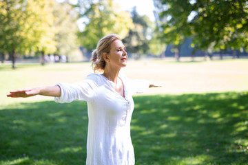 Eine attraktive Best-Ager Frau macht Meditations-Übungen im Park 