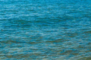 Obraz premium Clear water texture in blue and orange. Background of the ocean and the sea backlit by the sun. Soft waves. Natural water