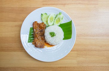 Rice and Pork Ribs On banana leaves With cucumbers on a white plate on wooden  table.