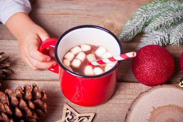 Child's hand holding red mug of Christmas cocoa on the wooden table