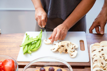 Cropped shot of person cutting mushrooms. Close-up partial view of people standing near table and preparing fresh healthy food. Healthy eating concept