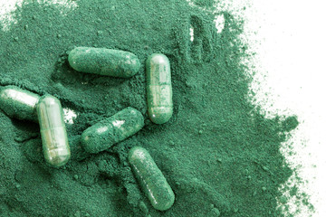 Pile of spirulina algae powder and capsules on white background.