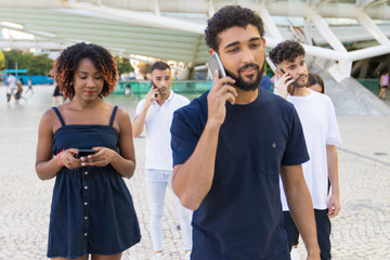 Group of people with cellphones standing in city square. Young mix raced men and woman walking outside, talking on cells, using mobile phones. Mobile phones using concept