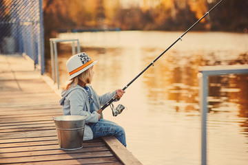 A little girl fishing from the pier on the pond in the Sunny morning.